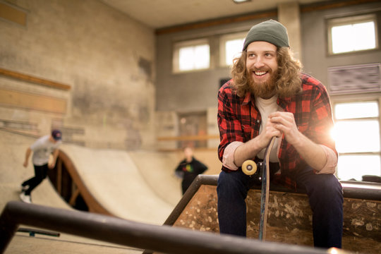 Portrait of long haired skater sitting on ramp in extreme park and smiling, copy space