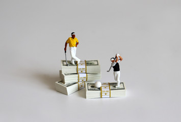 Miniature people playing golf with wad of $100 bills.