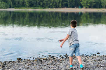 a child, a teenager, on a stony shore throws stones into the river, lake