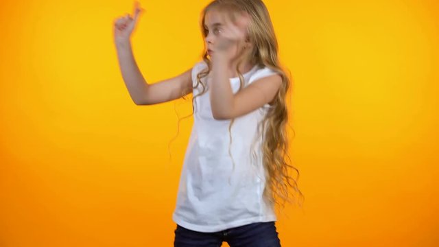 Funny preteen girl dancing, moving to music isolated on orange background
