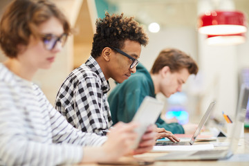 Busy students in computer class: serious concentrated young African-American student boy in glasses...