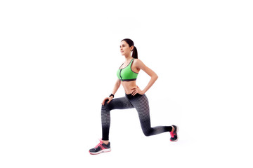Fototapeta na wymiar A young woman model in a sporty short top and gym leggings makes lunges by the feet forward, hands are held out to the side on a white isolated background in studio