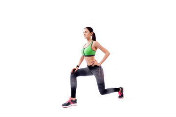 A young woman model in a sporty short top and gym leggings makes lunges  by the feet forward, hands are held out to the side   on a  white isolated background in studio