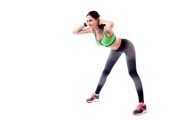 A young woman model in a sporty short top and gym leggings makes bends forward, arms behind head, legs wide apart  on a  white isolated background in studio