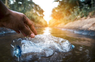The volunteer picking up a bottle plastic in the river , protect environment from a pollution concept.