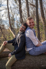 smiling two men, gay couple, leaning back to back, posing looking to camera carefree.
