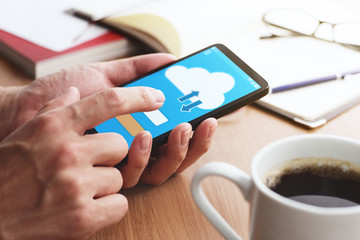 Closeup of male hands touching smartphone screen for using cloud app at table. Cloud app on...