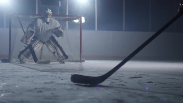 Unrecognizable hockey player preparing to shoot puck, goaltender standing in front of the net and waiting, then catching it with glove