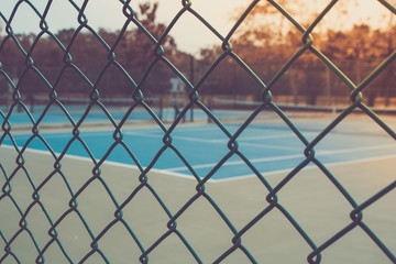 Fototapeta premium Close up metal fence with empty outdoor blue tennis hard court in the background. (Selective focus)