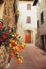 Fototapeta na wymiar Flores vermelhas, amarelas e laranjas em rua antiga com casas de pedra na Toscana 