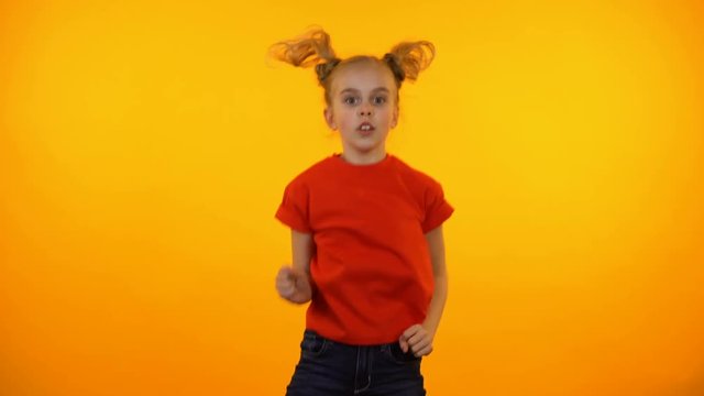Funny preteen girl dancing to music, active child having fun, orange background
