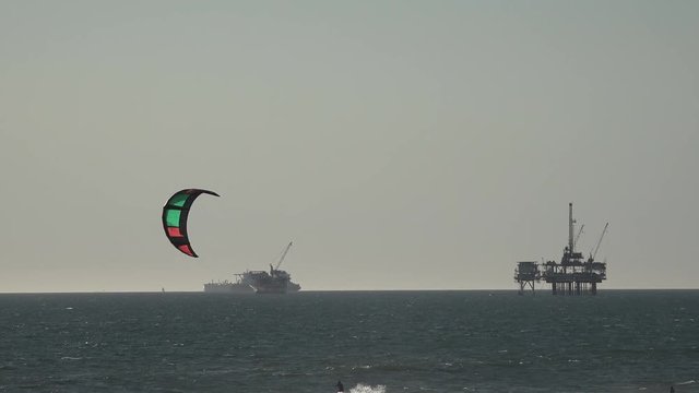 Parasailer passing by offshore oil drilling platforms in the Pacific ocean