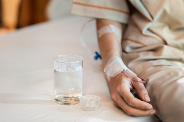 Asian man patient with medical drip or IV drip drinking water with medicine in hospital ward, Selective focus, Healthcare concept.
