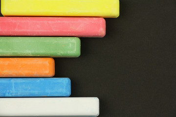 six colored children crayons on black background, on left side, blue red green yellow orange white, top view