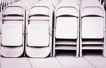 Dozens of fold up white metal chairs stacked .outdoor Party. - obrazy, fototapety, plakaty