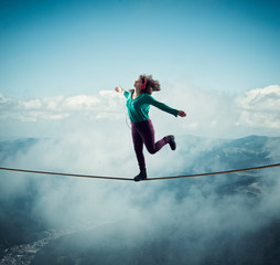 Woman balancing on a rope above clouds and mountains , while listening music . The concept of...