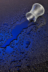 Glass of water spilled with drops on light background