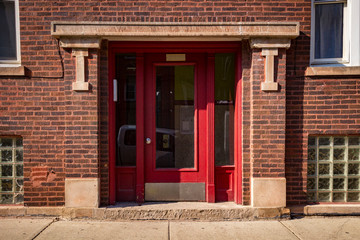 Entrance of a brick building with a red door in late afternoon