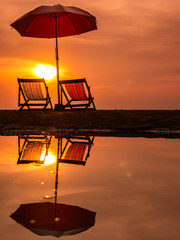 Sunrise with orange morning sky with chair and umbrella on beach reflection in water