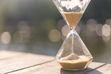 Hourglass clock on white wooden table with bokeh sunset light of lake abstract background.