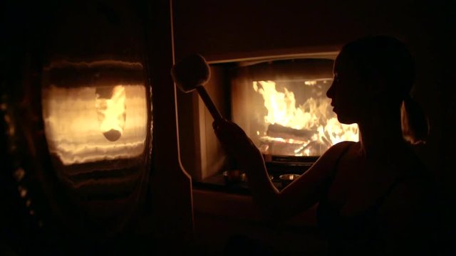 woman is hitting gong in mystical dark space with burning fire in background