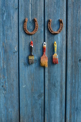 Hang on blue old wall two rusty horseshoe and three brushes