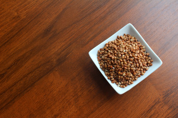 White Bowl with grains of buckwheat on a wooden table, top view. Photo with empty place for text.   
