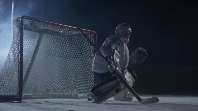 Concentrated male hockey goaltender standing on ice rink and stopping puck with stick to prevent it entering the net