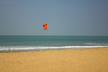 a red flag in the wind meaning swimming is prohibited, on a yellow sandy beach against the turquoise ocean under a clear blue sky
