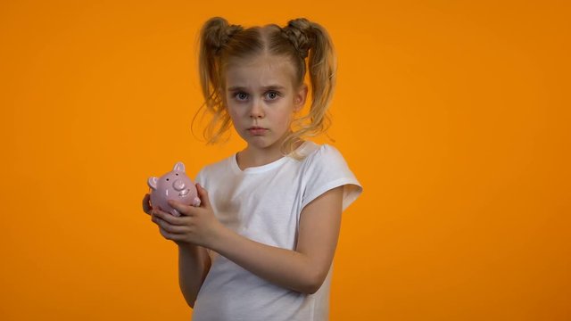 Displeased cute girl shaking piggybank, no money, insufficient savings, spender