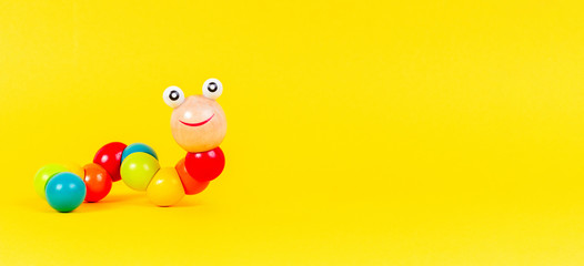 Colorful wooden baby toy worm on yellow background