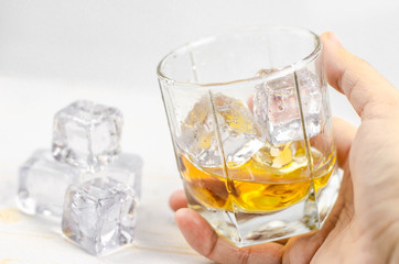 Glasses of scotch whiskey with ice cubes, white background, wooden backdrop