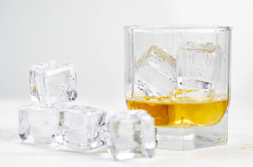 Glasses of scotch whiskey with ice cubes, white background, wooden backdrop