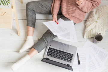 Young woman sits on the floor in a Scandinavian apartment interior with a laptop, studying law, freelance girl at work, distance learning student, online employment, paperwork and outsourcing concept - obrazy, fototapety, plakaty