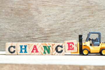 Toy forklift hold letter block E to complete word chance on wood background