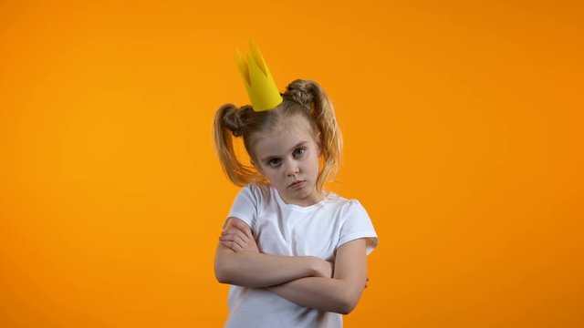 Naughty girl in paper crown with hands crossed on chest frowning, awkward age