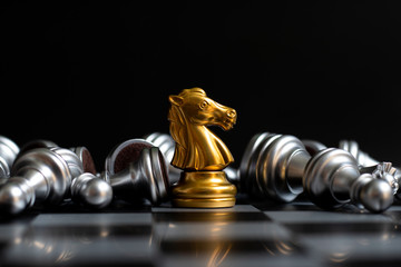 Gold knight chess piece win over lying down pawn on black background