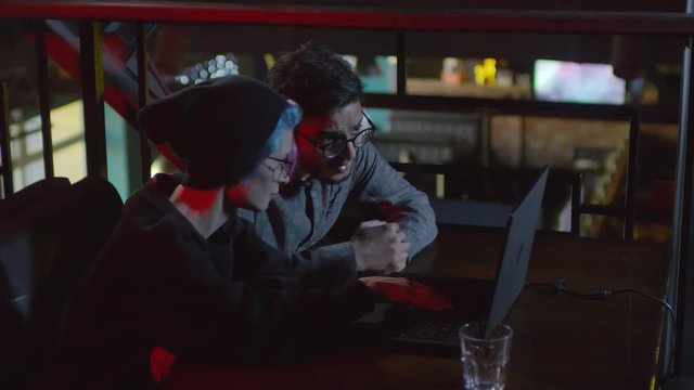 Lockdown of young man and woman sitting at caf&eacute; table and using laptop together