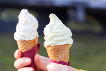 Woman's hands holding melting ice cream waffle cone in hands on summer light nature background