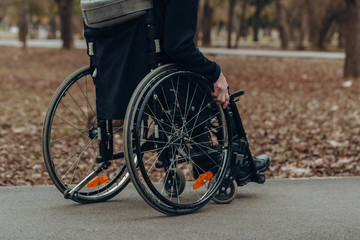 Close-up of male hand on wheel of wheelchair during walk in park