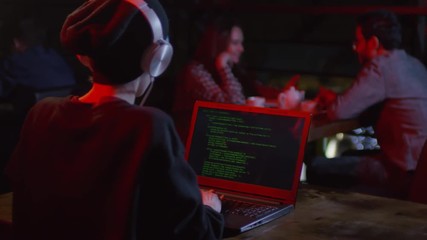 Rare view of young woman sitting at computer in bar and developing new computer program