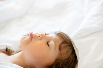 Adorable little sad girl lying in the bed in the early morning