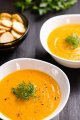 Pumpkin cream soup with croutons and fresh dill and parsley on dark wooden background, top view