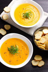 Pumpkin cream soup with croutons and fresh dill and parsley on dark wooden background, top view