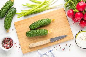 Cooking in kitchen, empty cutting board, ingredients of spring salad around, cucumber, green onion and radish