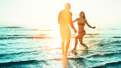 happy young multicultural couple playing in sea on a beach vacation on honeymoon destination. silhouette image with colorful sunset background with warm color effects of light leaks