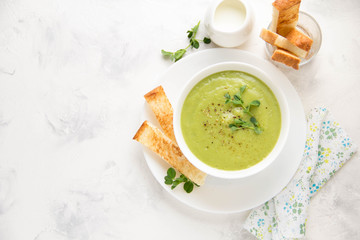 Green cream vegetable soup broccoli, peas, zucchini, spinach) with toast, croutons. Delicious vegetarian healthy spring, summer food on light background