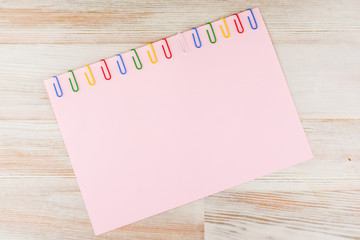 A sheet of pink paper fixed with multi-colored paper clips on a light Board table in a diagonal turn