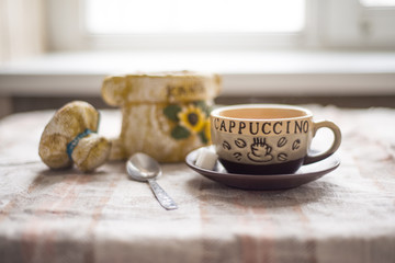 the coffee Cup on a linen tablecloth on the background of the window, the coffeepot and spoon in a blur in the background