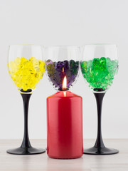 creating an intimate atmosphere, room decoration: red candle on the background of three glasses filled with hydrogel balls of different colors